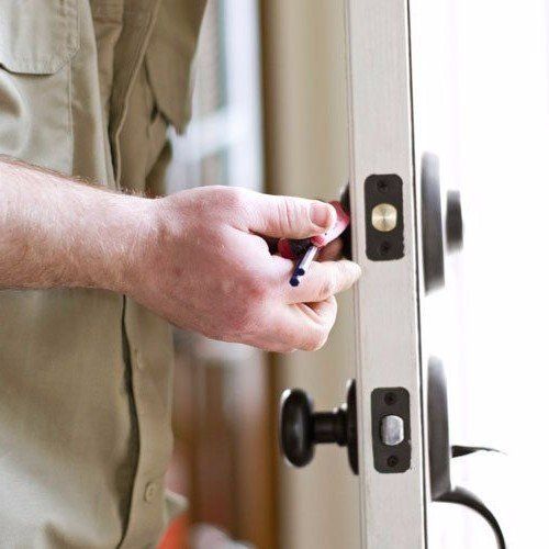 A man is fixing a door with a screwdriver and a key.