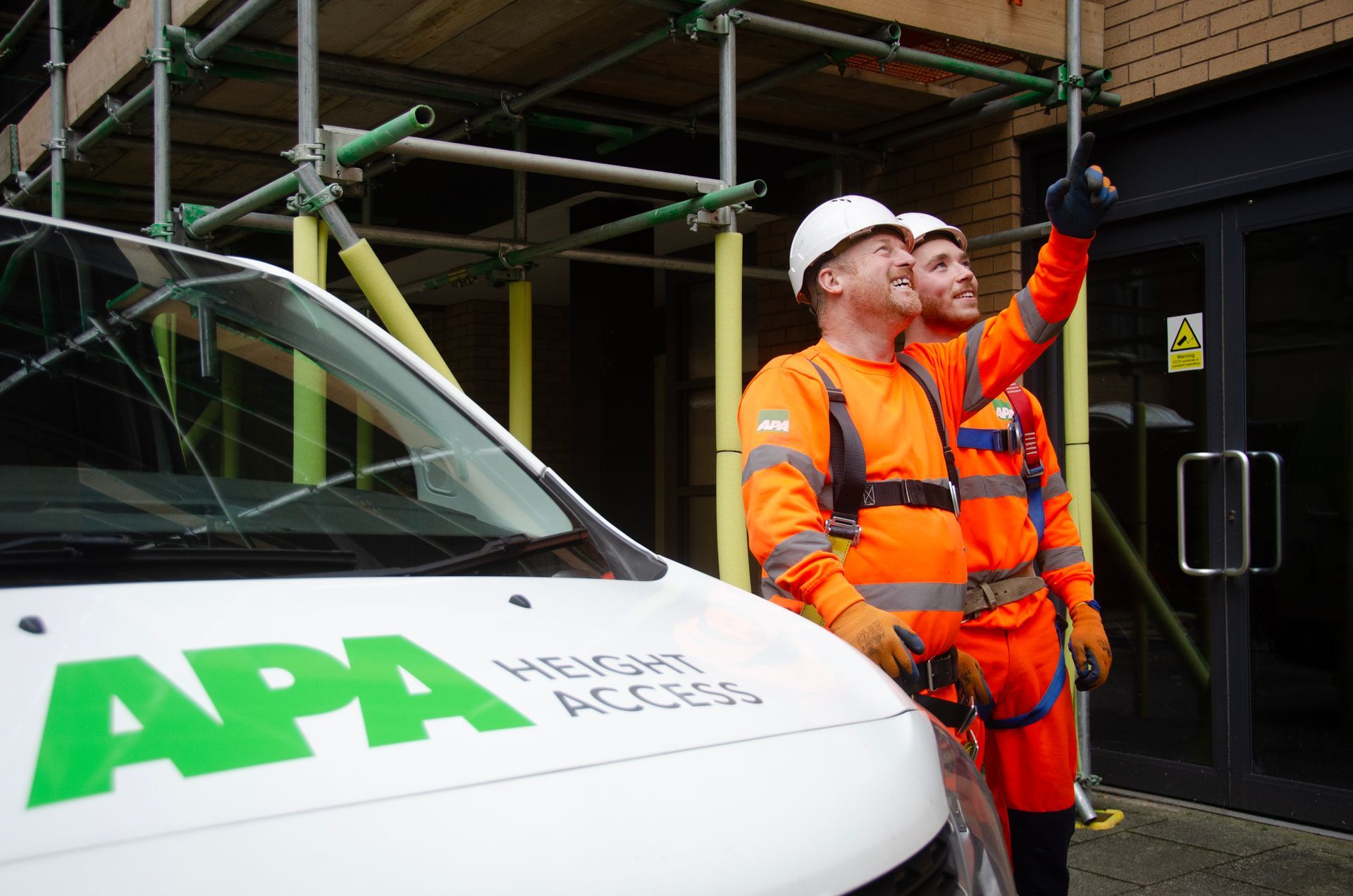 Two APA Height Access team members are standing next to a white van that says APA on it.