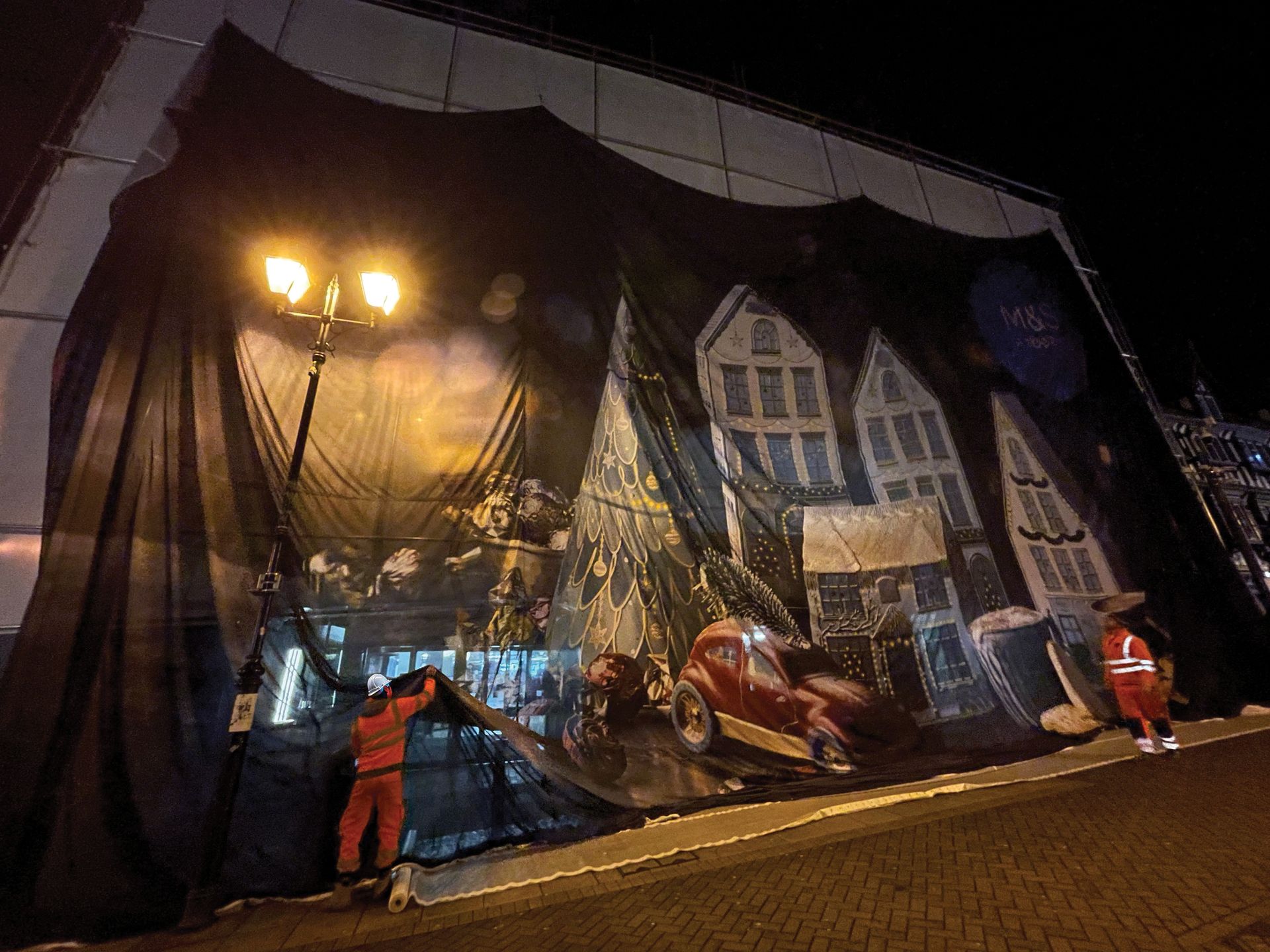 A large black tarp is covering a building with a painting of houses on it.