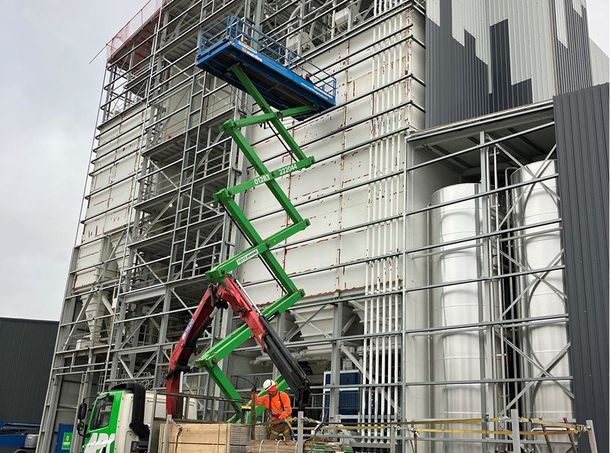 A man is standing on a scissor lift in front of a large building.