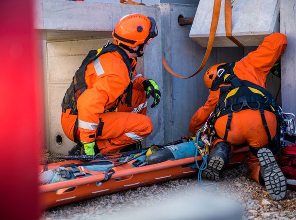 A man wearing an orange vest with the word apa on it is standing on a scaffolding.
