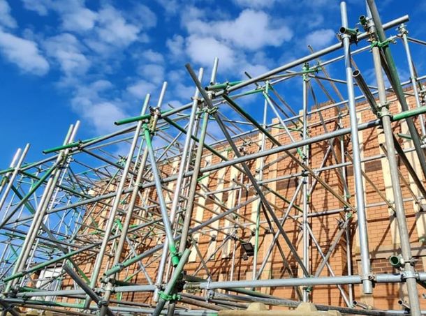 A large building is being built with scaffolding and a crane in the background.