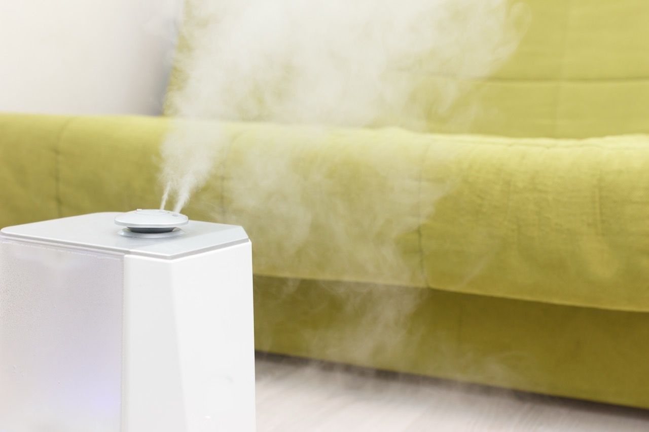 Blue tabletop humidifier on a wooden table in front of a brown couch with a coral pillow.