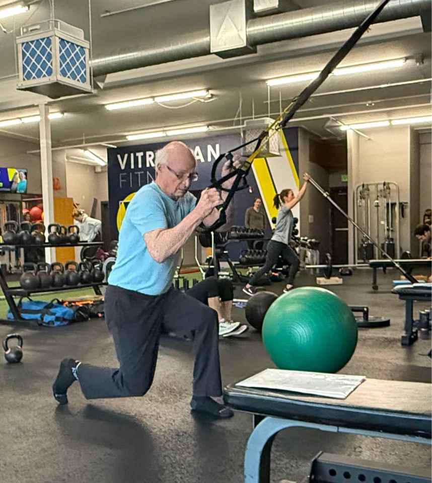 A man performing a TRX Assisted Lunge and a woman performing a Landmine Shoulder Press