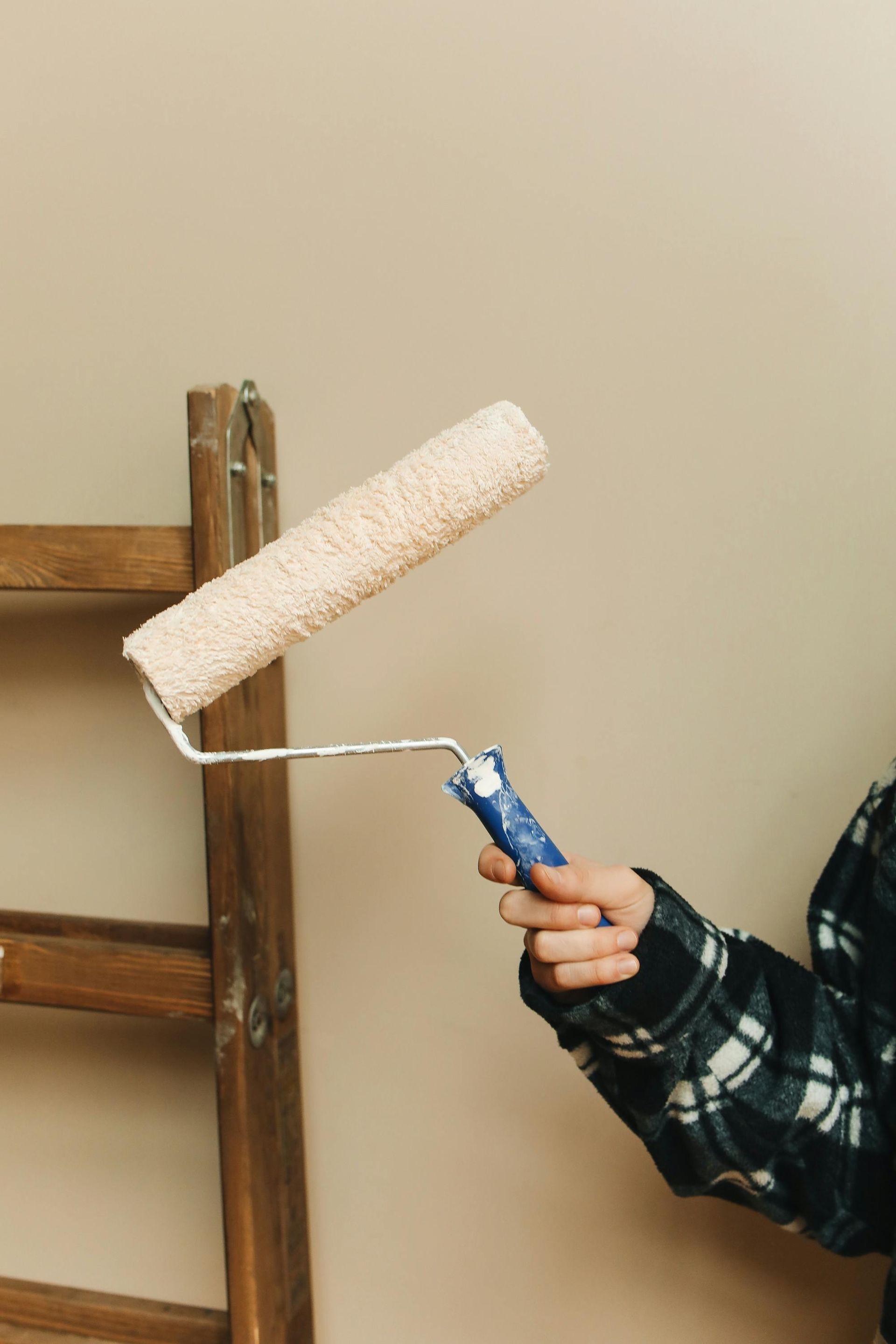 A person is holding a paint roller in front of a wooden ladder.