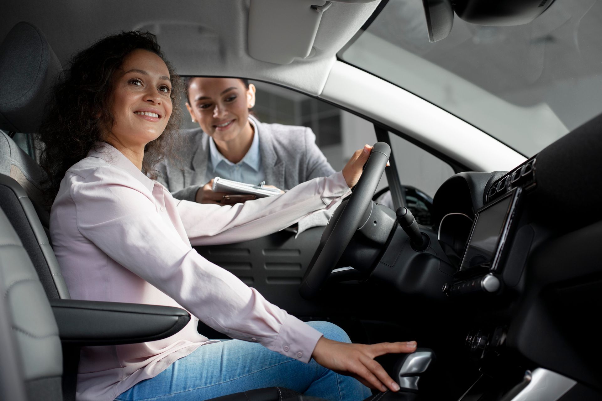 A smiling driver in a blue shirt holds up a driver's license, giving a thumbs up alongside an instructor in a car.