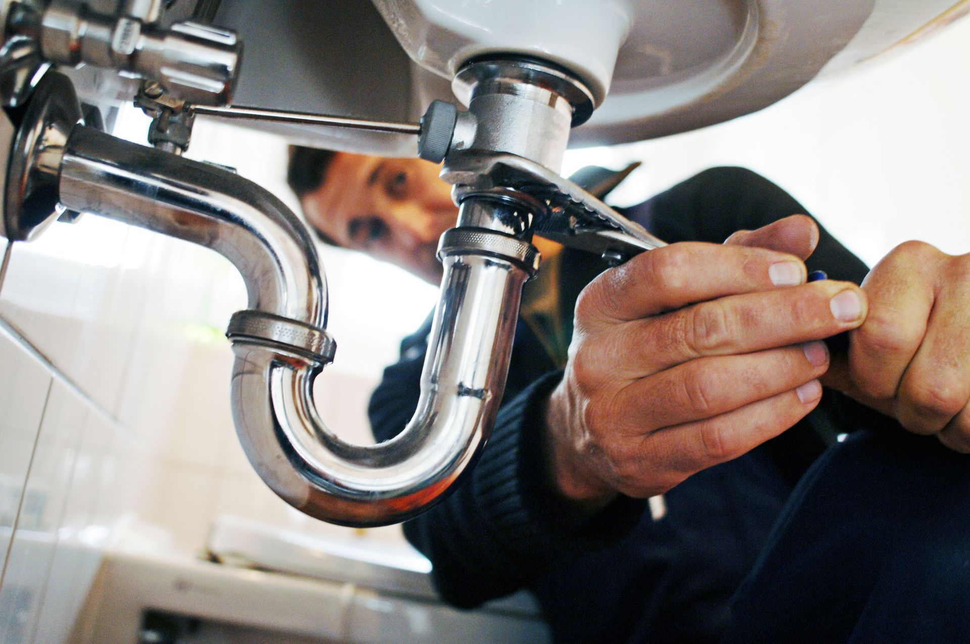 Plumber tightening a pipe under a sink with a wrench; close-up.