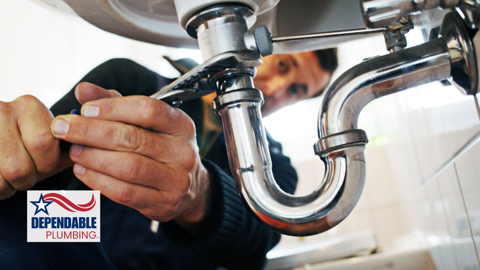 Plumber using a wrench to work on a sink's pipes.