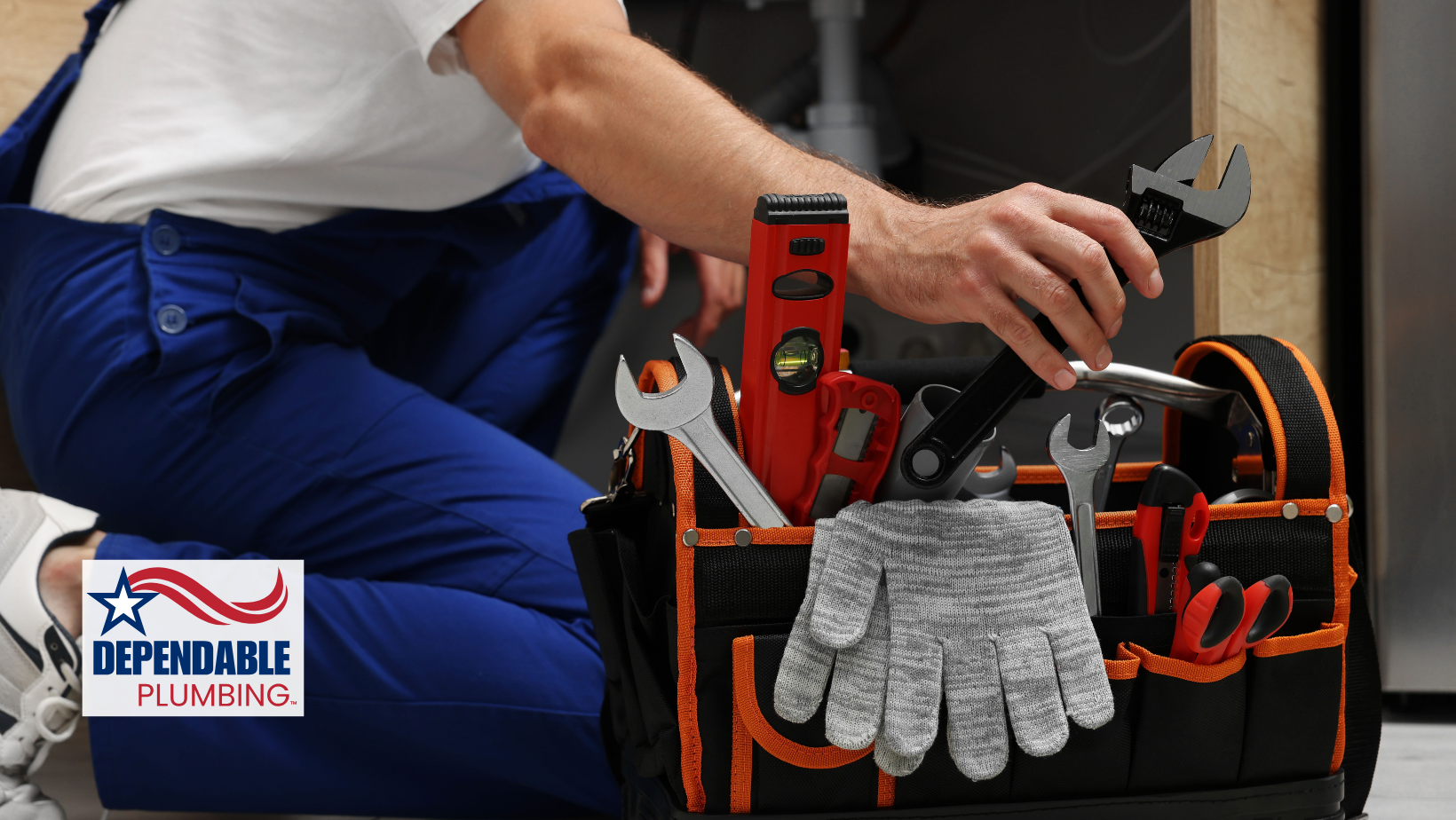 Plumber with tool bag, kneeling near plumbing work; blue overalls, tools, gloves.
