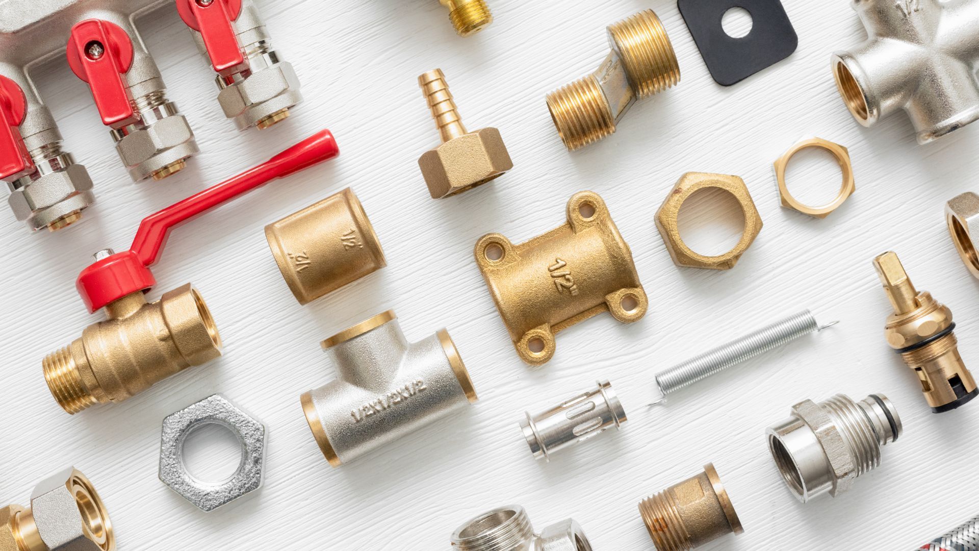Plumbing fittings: brass and metal pipes, valves, connectors, and joints arranged on a white surface.