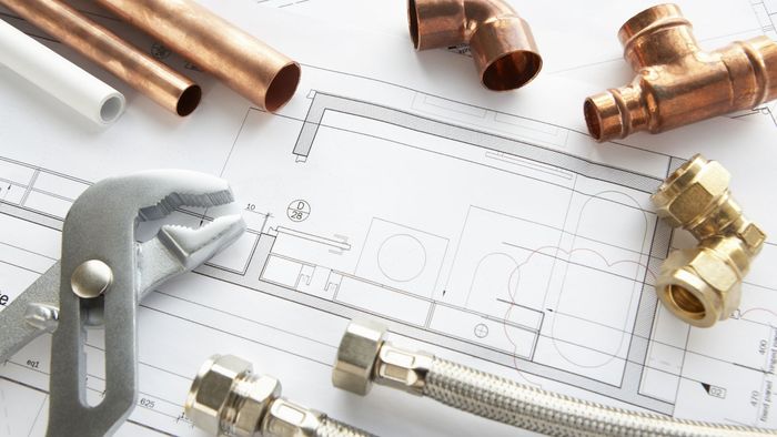 Plumbing tools and copper pipes on a blueprint, including a wrench and connector fittings.
