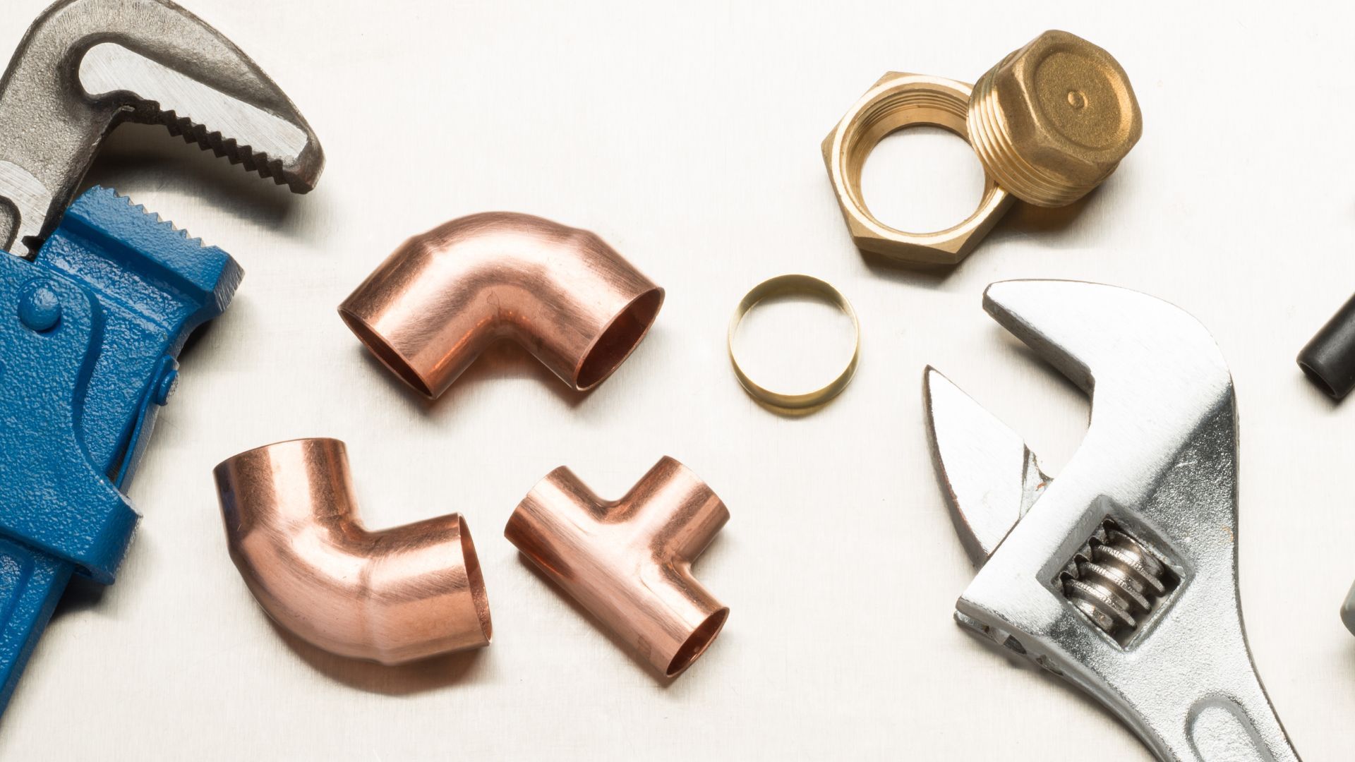 Plumbing tools and copper fittings arranged on a white surface, including wrenches and elbow joints.