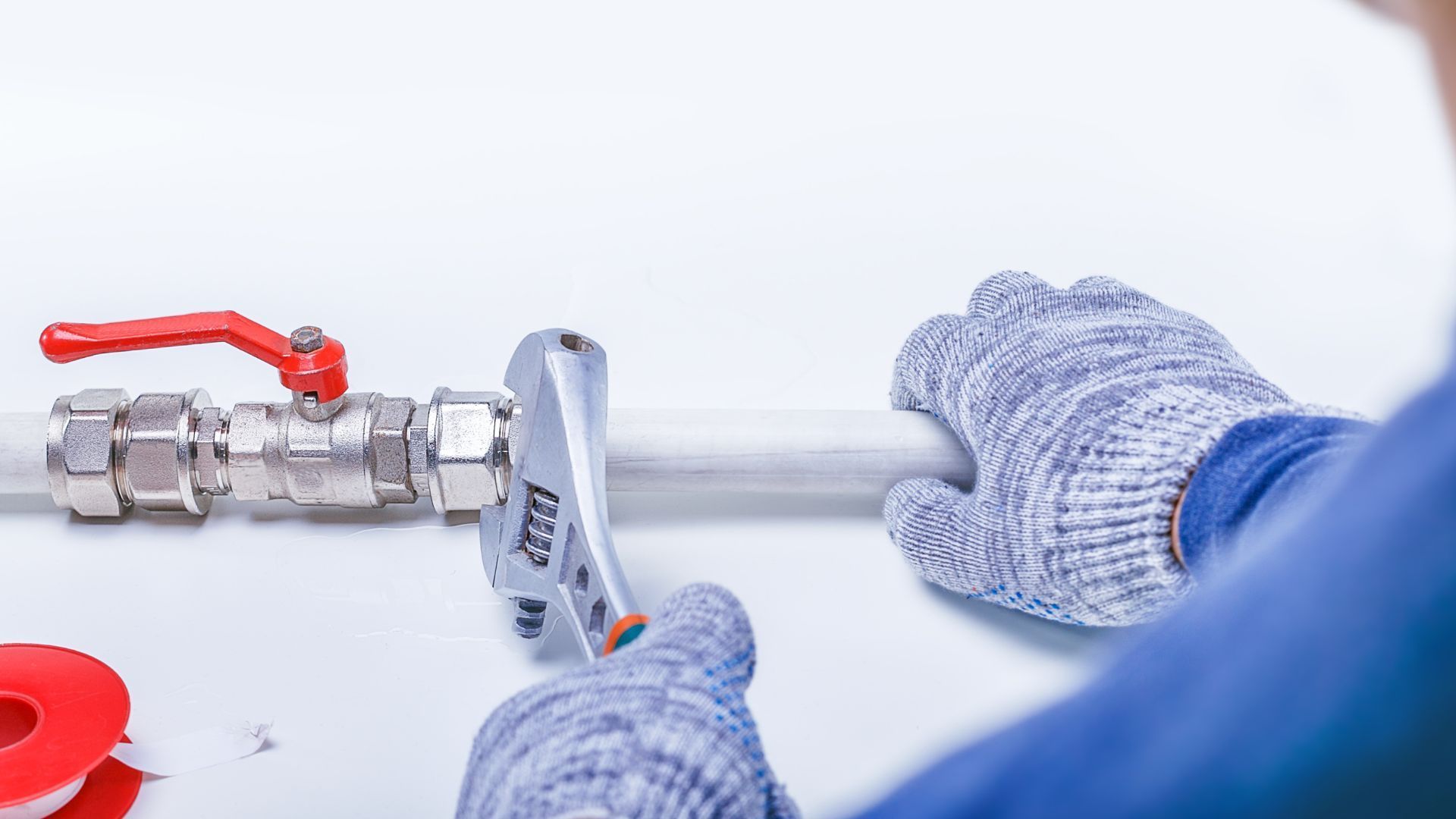 Plumber with a wrench working on a pipe near a red valve.