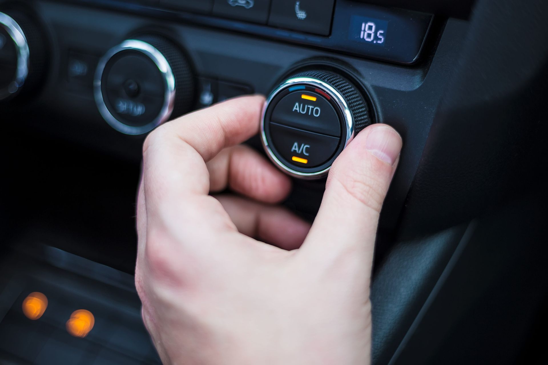 Driver adjusting the car's air conditioning controls to maintain a comfortable cabin temperature.