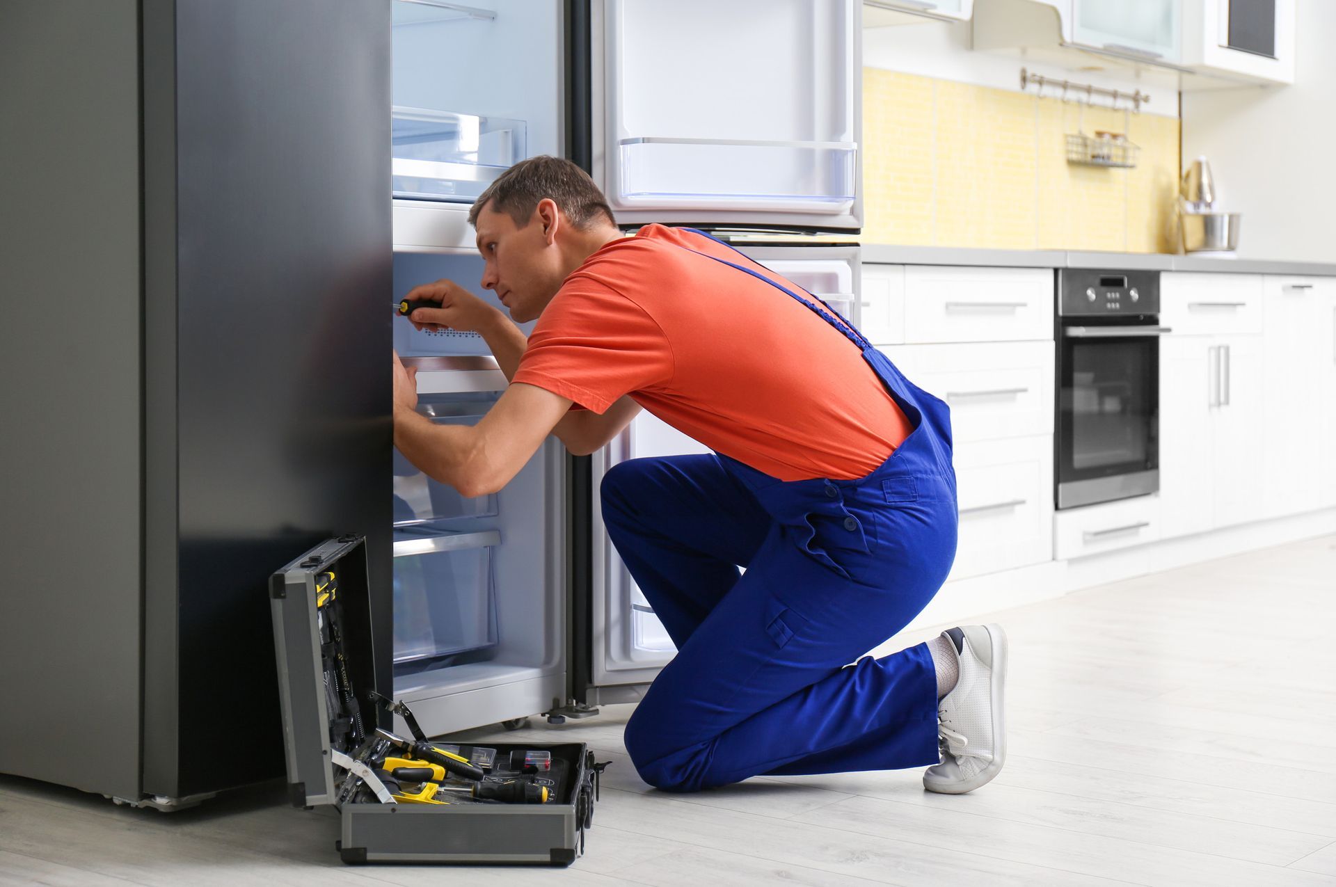 A man is fixing a refrigerator in a kitchen.