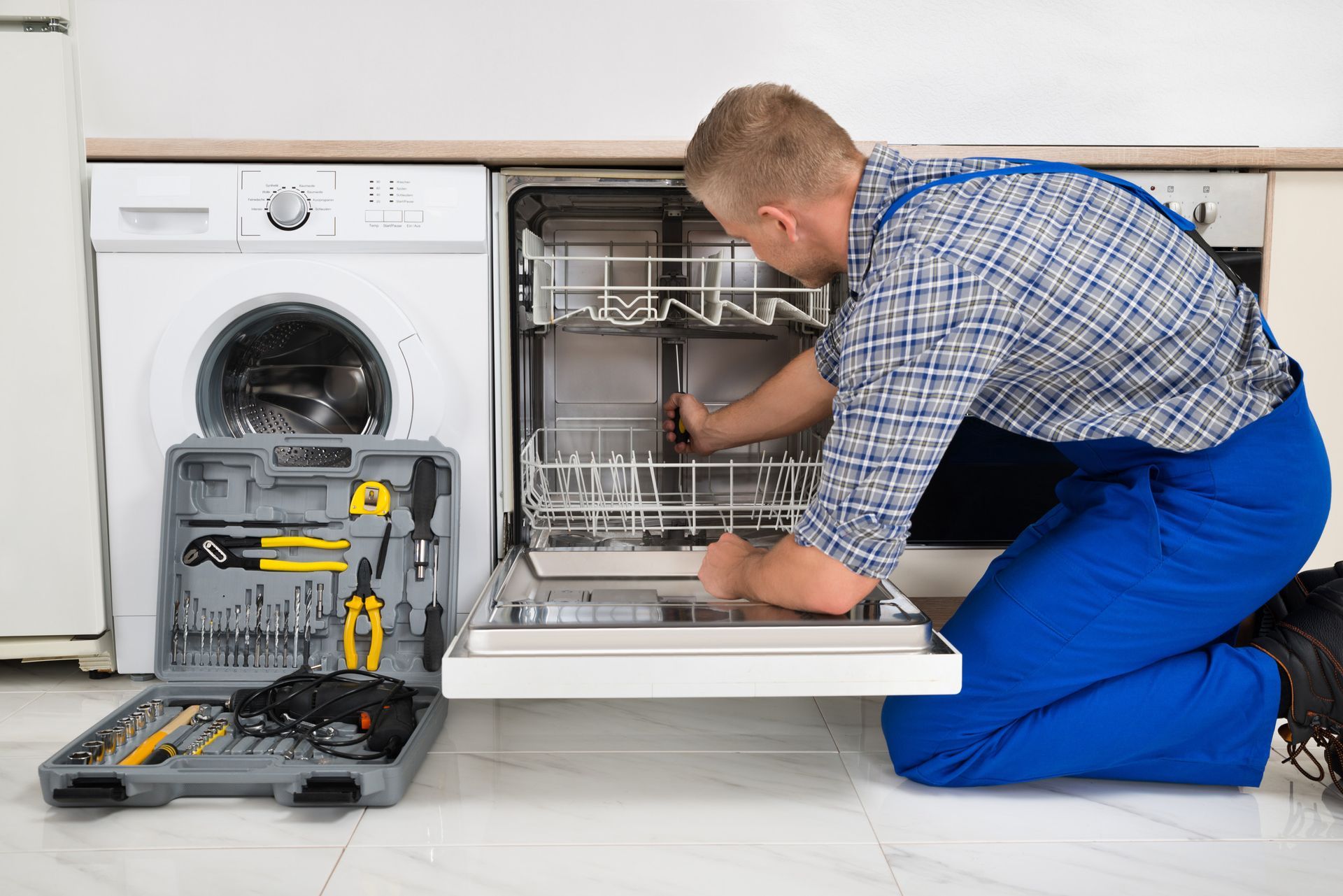 A man is kneeling down fixing a dishwasher in a kitchen.