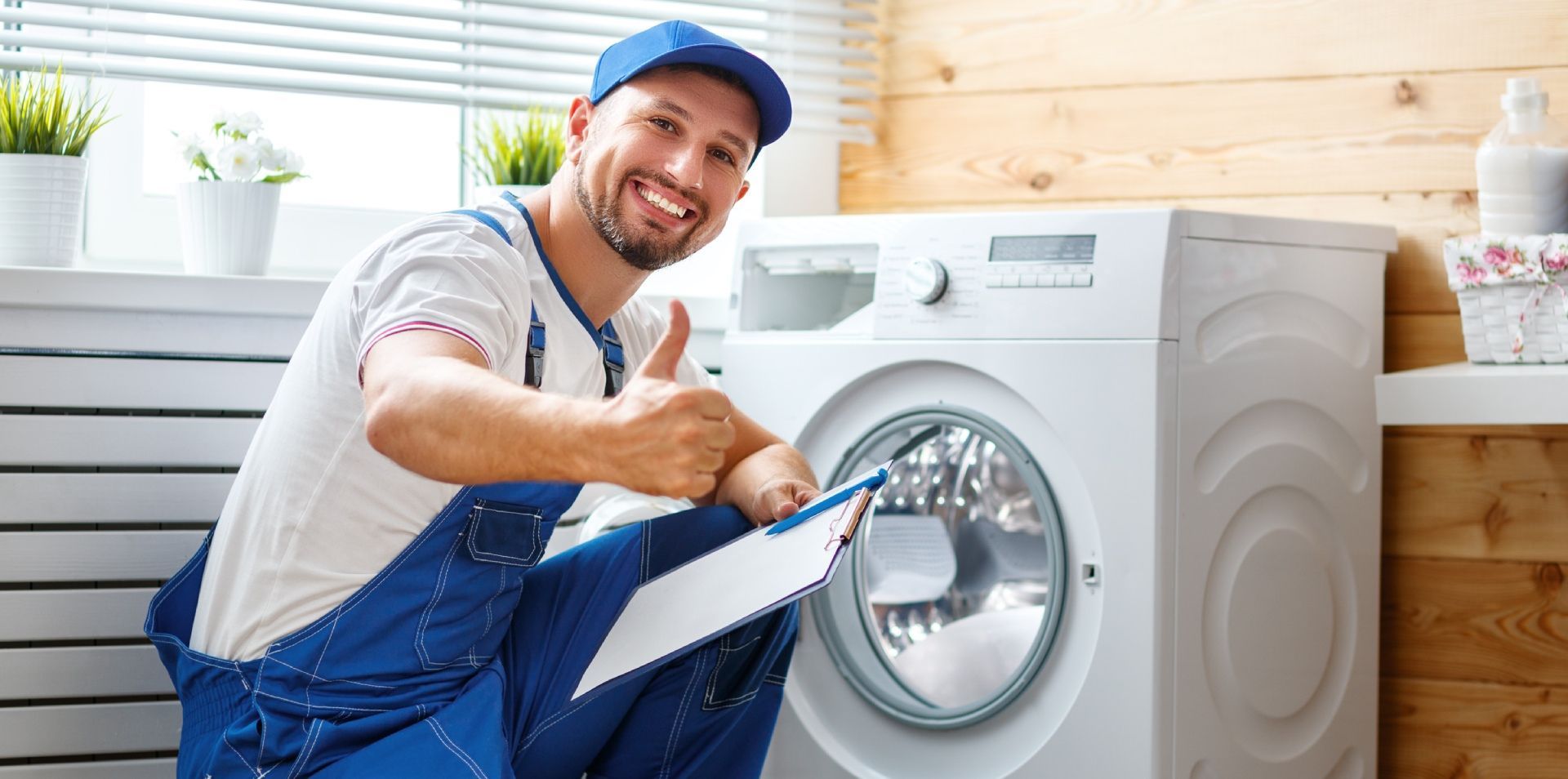 A man is fixing a washing machine and giving a thumbs up.