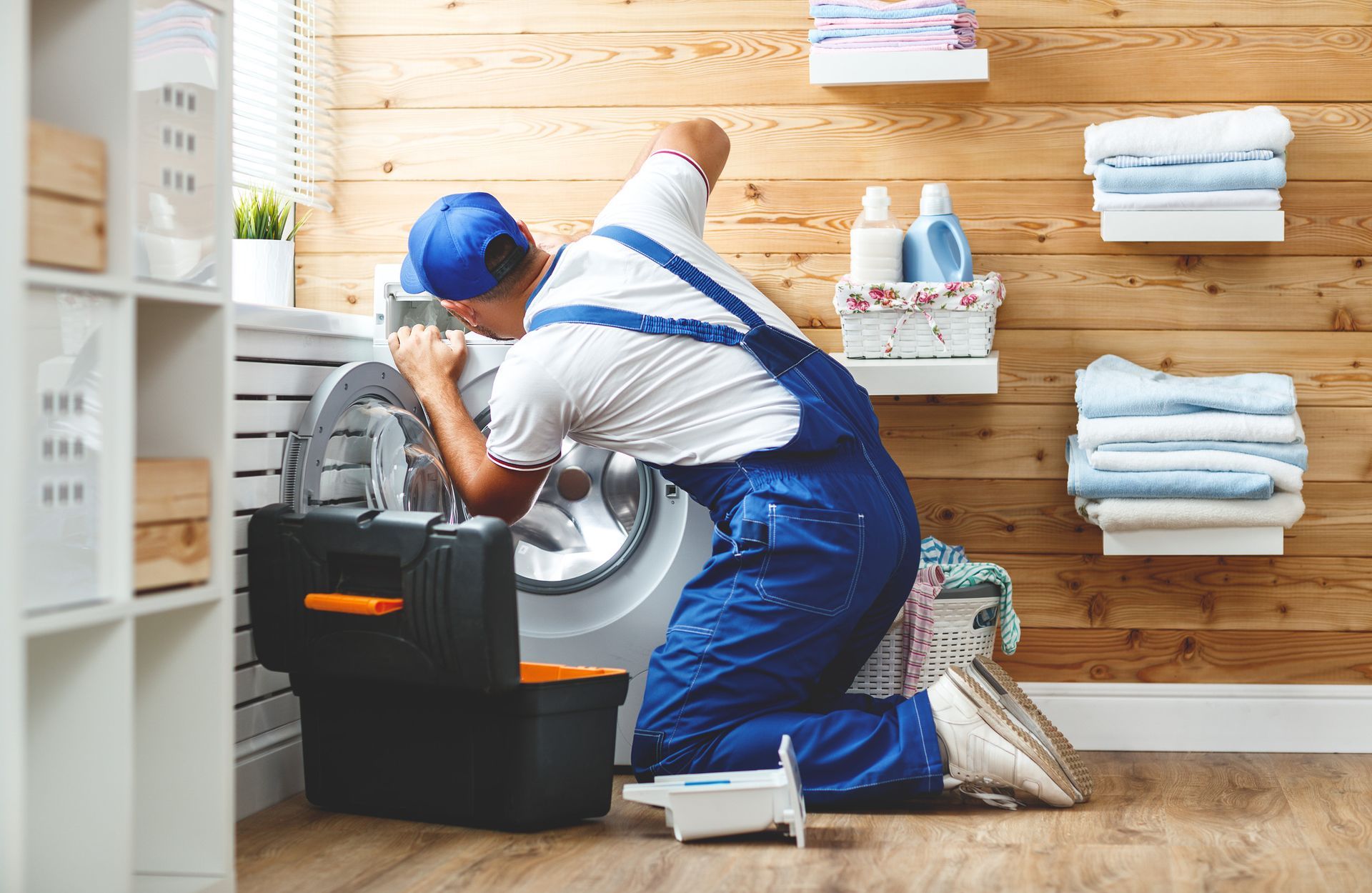 A man is fixing a washing machine in a laundry room.