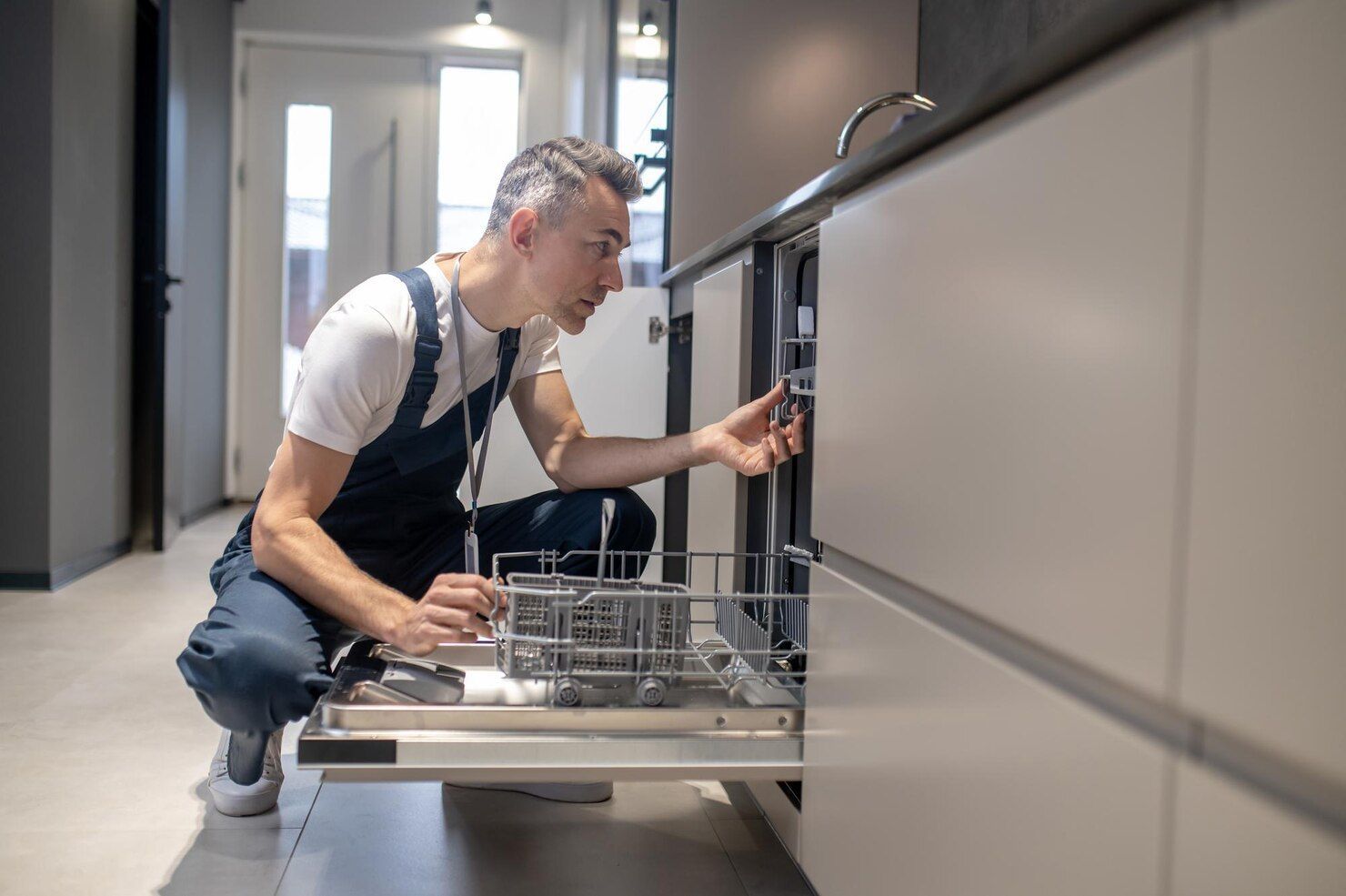 A man is fixing a dishwasher in a kitchen.
