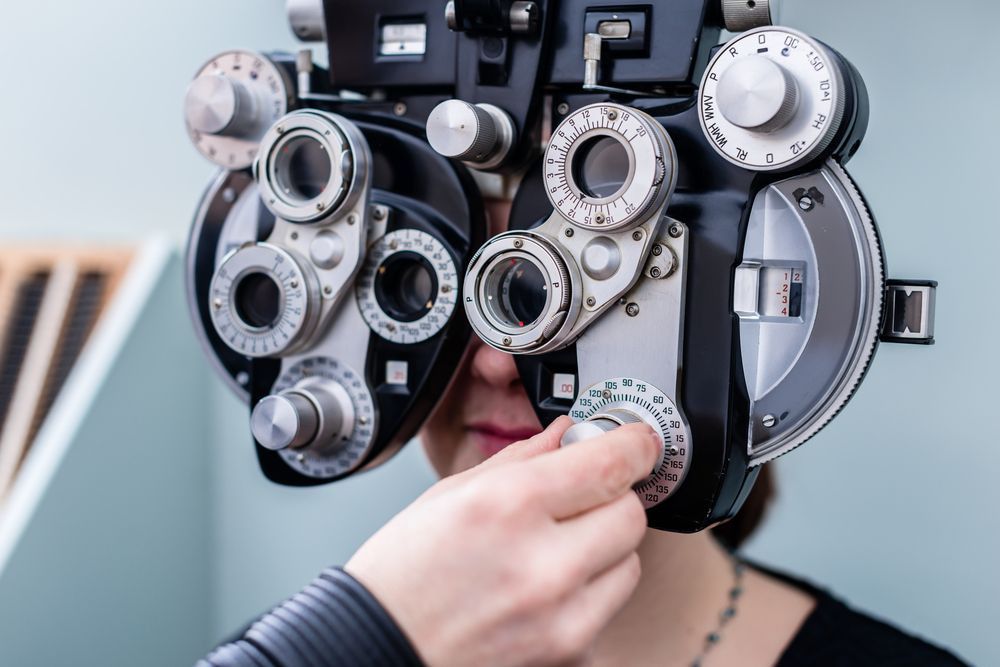 A Person's Eye Exam with A Phoropter Hand Adjusts Dial on The Black Medical Device — Eyepower In Tahmoor, NSW