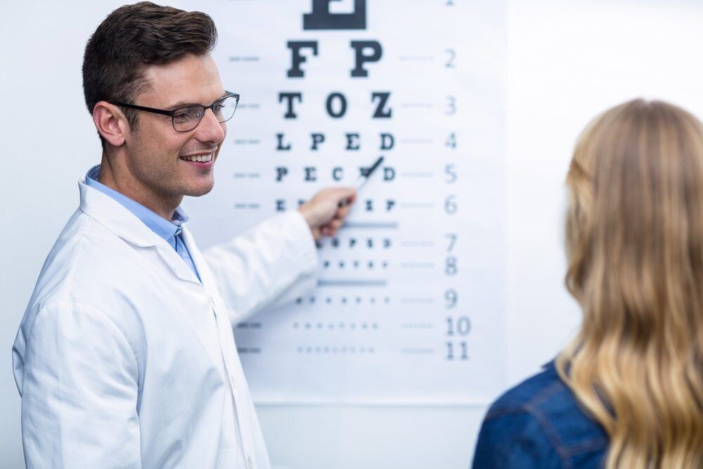 An Ophthalmologist is Talking to a Woman in Front of an Eye Chart — Eyepower In Tahmoor, NSW