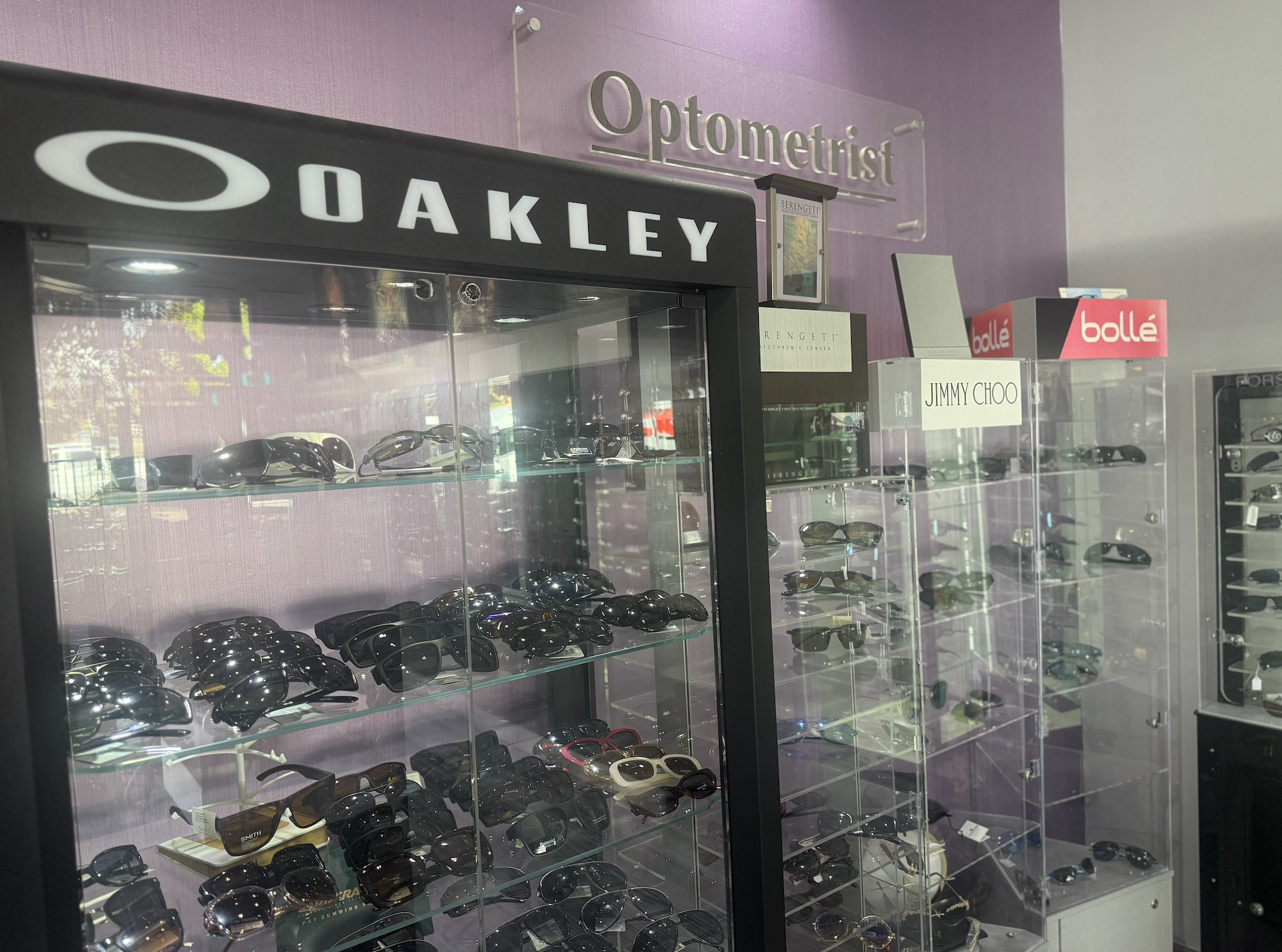 Sunglasses displayed in a store. Oakley cabinet on left, other brands in glass cases  — Eyepower In Tahmoor, NSW