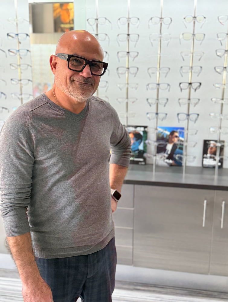 Man with glasses smiles in an optical shop, poses in front of a wall of frames  — Eyepower In Tahmoor, NSW