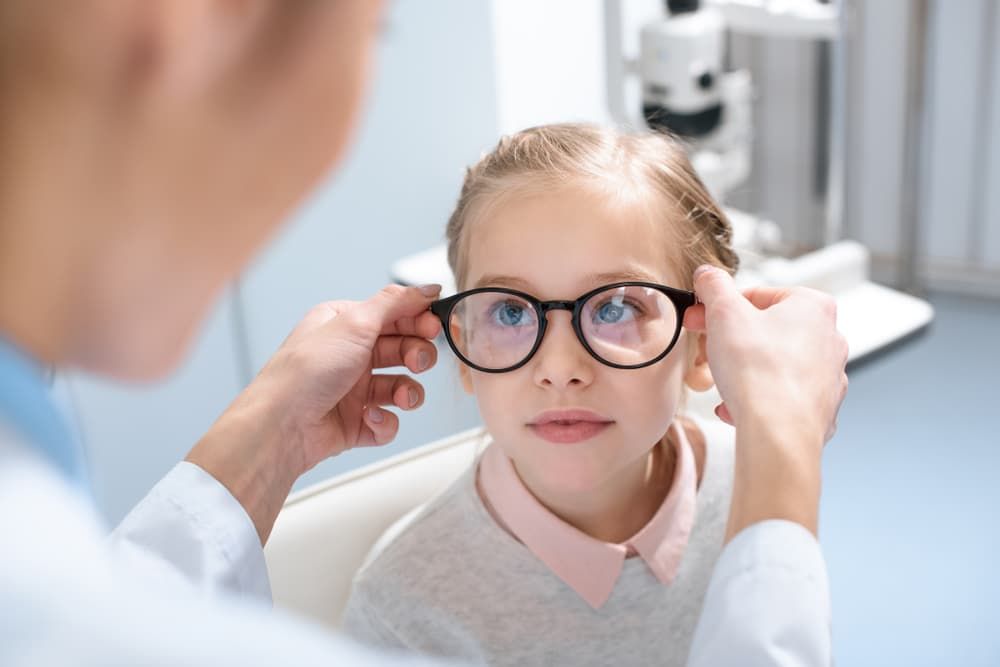 An optometrist fitting eyeglasses on a young girl in a clinic setting — Eyepower In Tahmoor, NSW