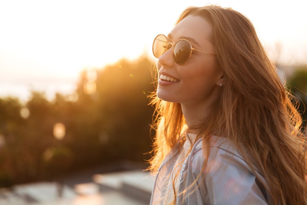 Woman with sunglasses smiles in golden sunlight — Eyepower In Picton, NSW