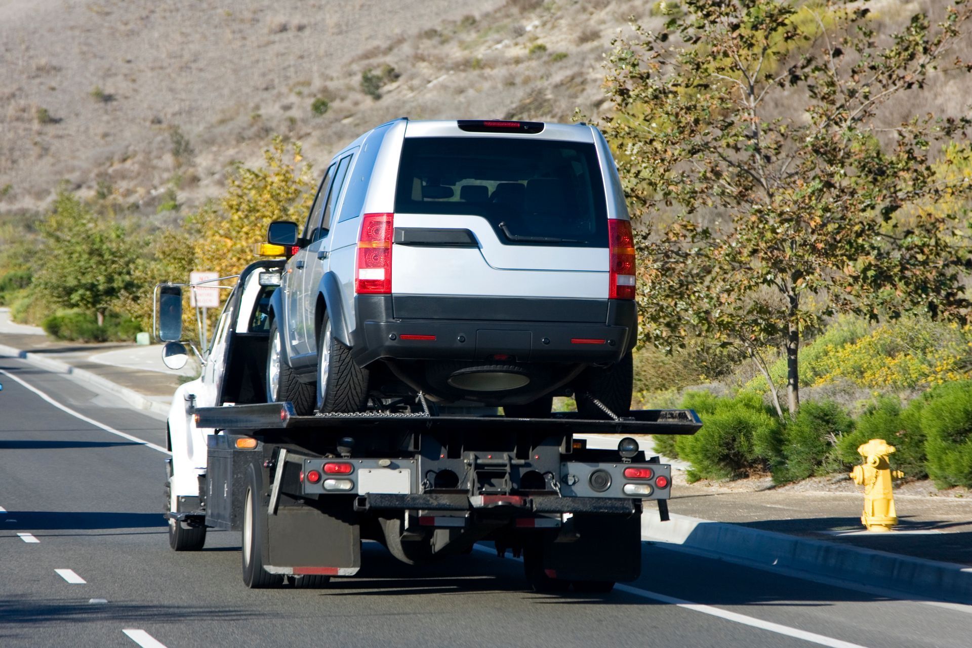 A tow truck is towing a suv down the road.
