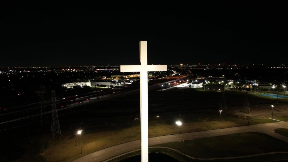 Night drone photo of an illuminated cross above city lights