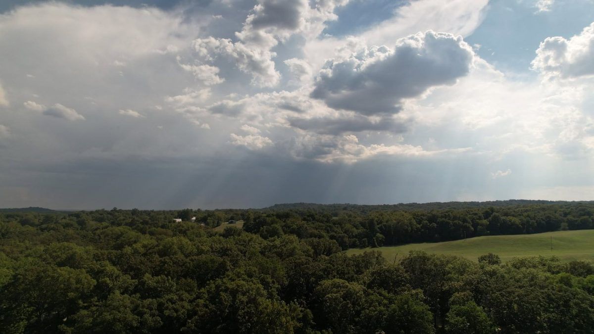 Aerial photo of sun rays breaking through clouds over farmland and forest