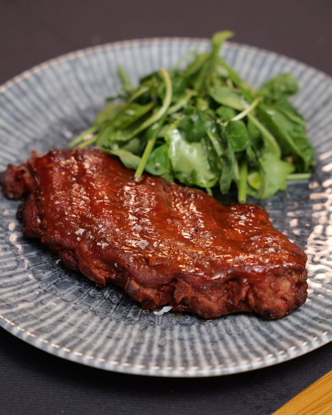 Bistecca grigliata glassata con insalata verde su un piatto grigio decorato.