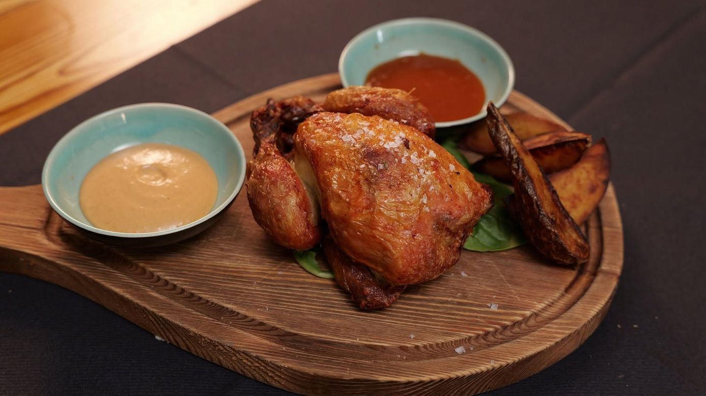 Pollo arrosto su un piatto di legno con due salse in ciotole blu.