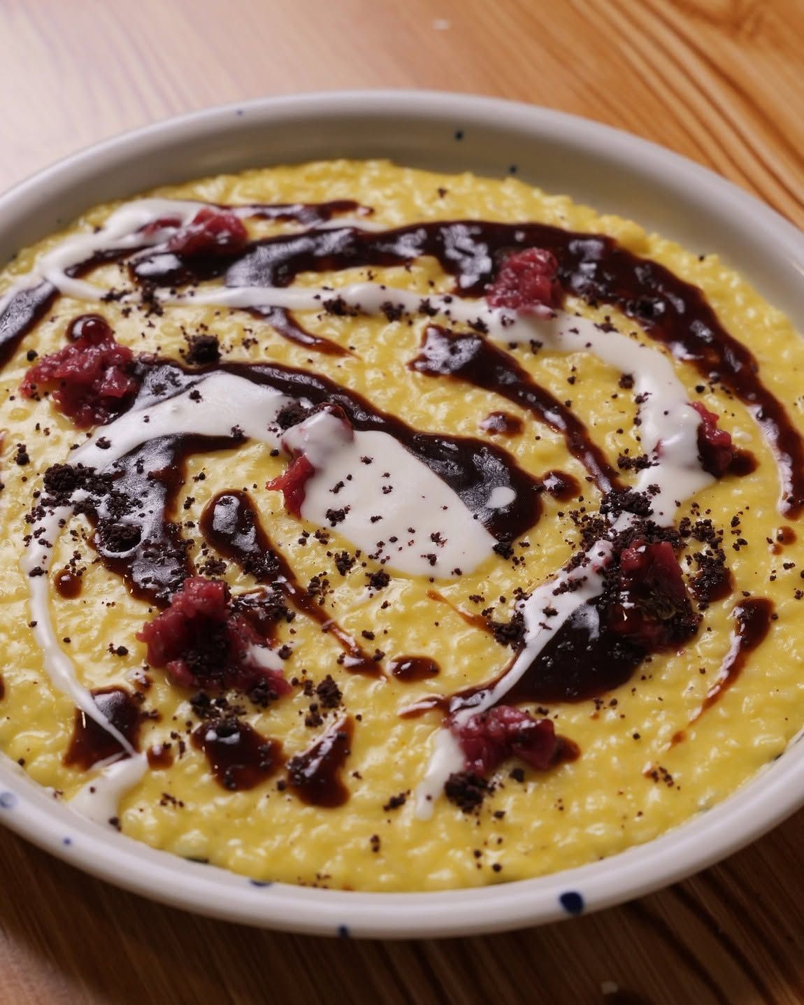 Risotto cremoso giallo con una spruzzata di cioccolato e frutti di bosco sparsi, servito su un piatto bianco.