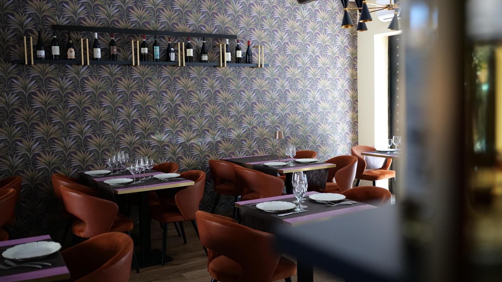 Tavoli vuoti da caffè con sedie blu e bicchieri da vino in una sala da pranzo luminosa e illuminata da luci soffuse.