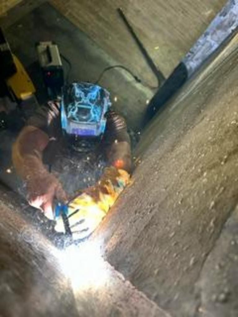 Worker welding inside a narrow concrete shaft, bright sparks lighting the dark space