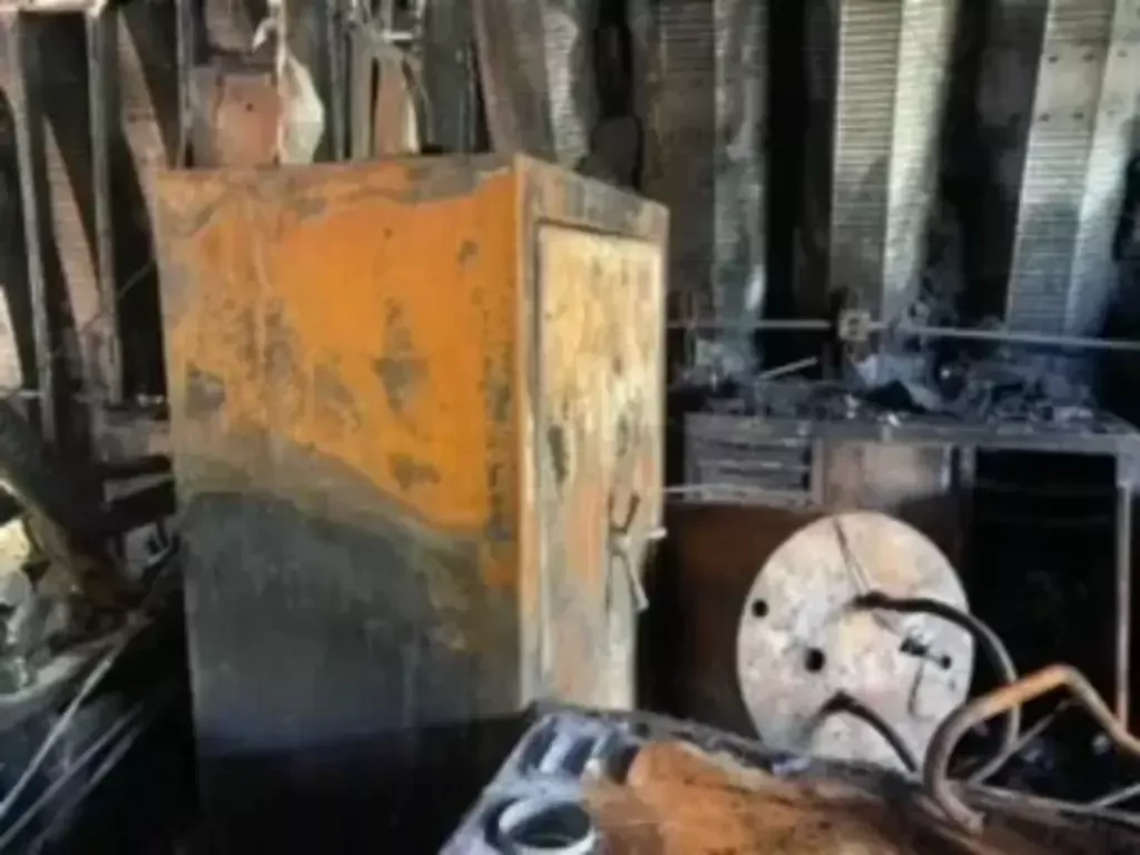 Charred industrial machine and debris inside a damaged, soot-blackened room