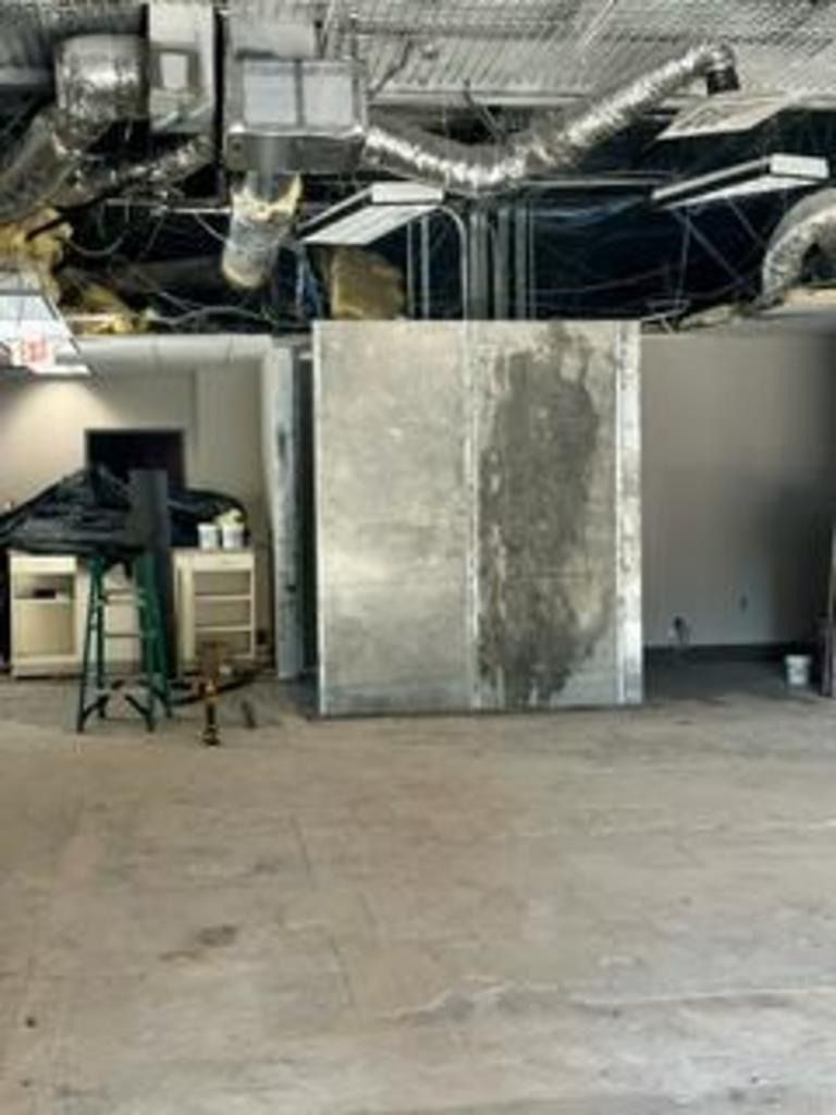 Empty industrial interior with exposed ceiling ducts, a large metal panel, and storage items on the left.