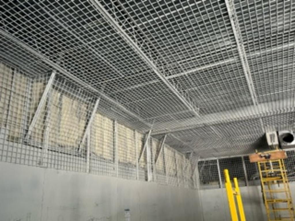 Industrial interior with wire-mesh ceiling and walls, yellow scaffold, and large gray tank or chamber