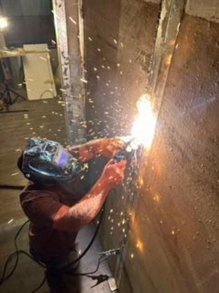Worker welding metal in a narrow industrial space, with bright sparks flying.
