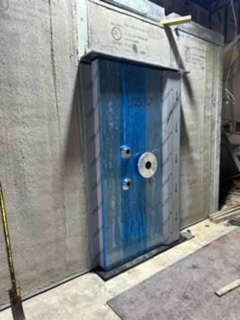 Blue industrial door set in a concrete wall, with a round handle and metal paneling.