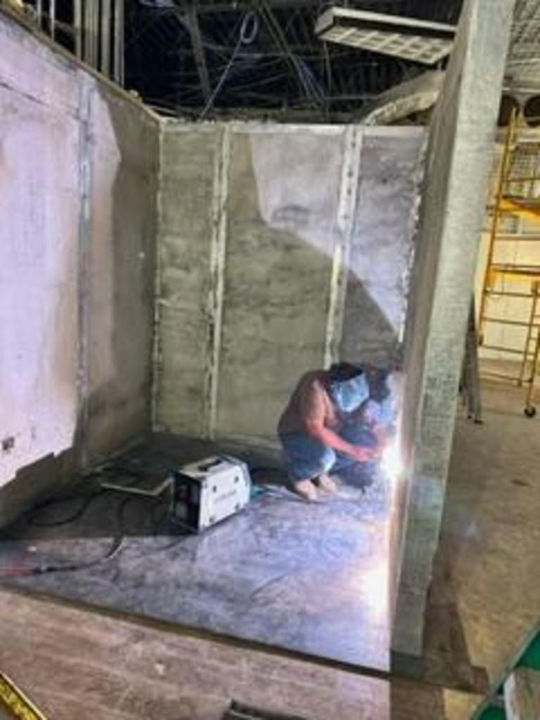 Worker welding inside a concrete room under construction, with sparks and a power unit on the floor