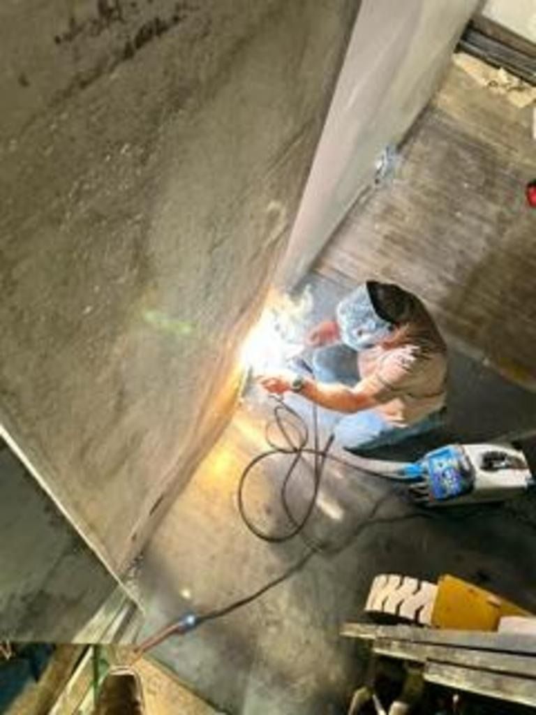Worker welding a concrete wall indoors, with bright sparks and tools on the floor.