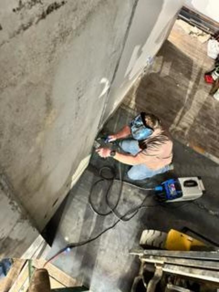 Worker in a blue mask using a power tool on a concrete wall in a narrow construction area.