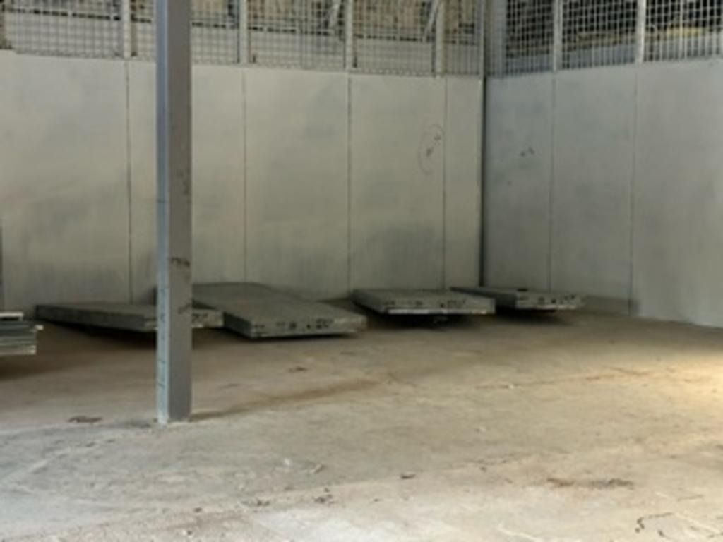 Empty warehouse with concrete floor, metal support post, and flat pallets or platforms along the back wall