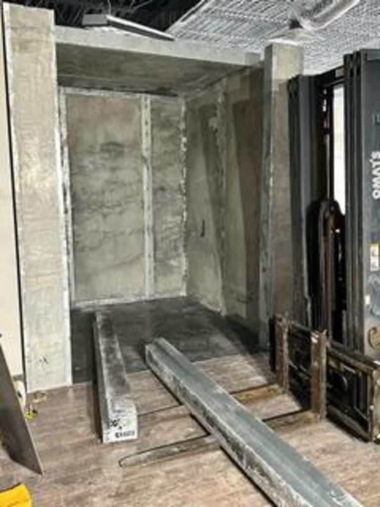 Concrete elevator shaft with two metal beams and a black gate in a construction area