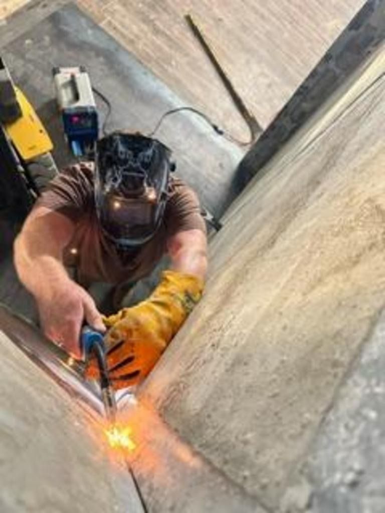 Worker welding inside a narrow concrete shaft, sparks flying from the torch