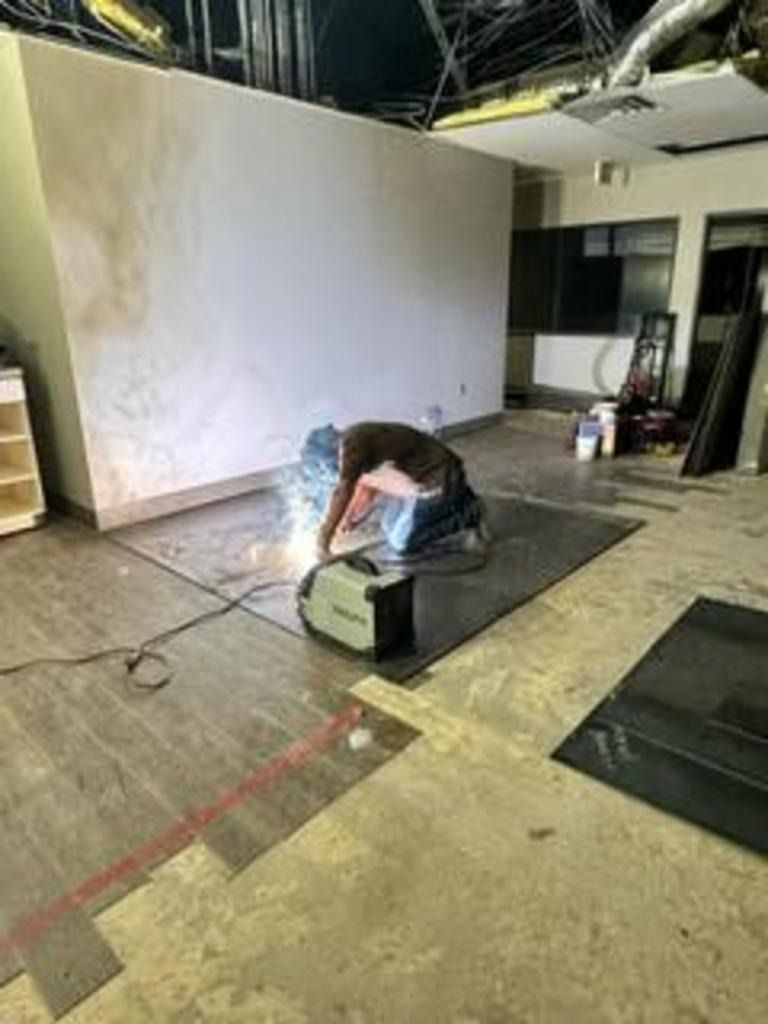 Worker welding on a metal piece in a large unfinished industrial room