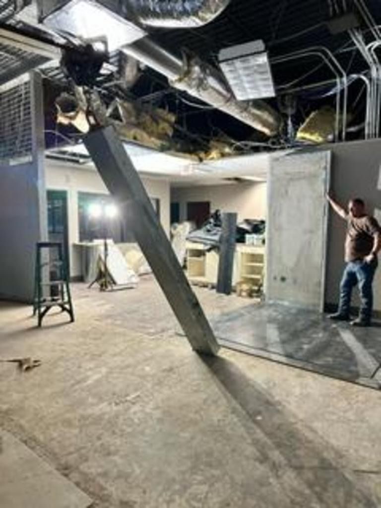 Damaged office interior with a collapsed ceiling, debris, and a person inspecting the scene.
